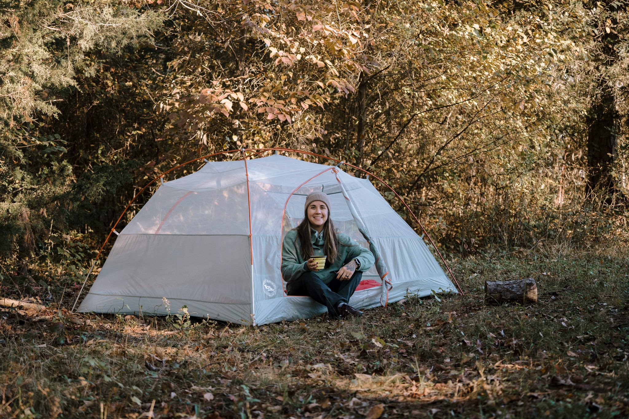 Bethany, the author of this post, sits in a camping tent holding a Sea to Summit collapsible bowl. One of the items in this list of camping gear suggestions!
